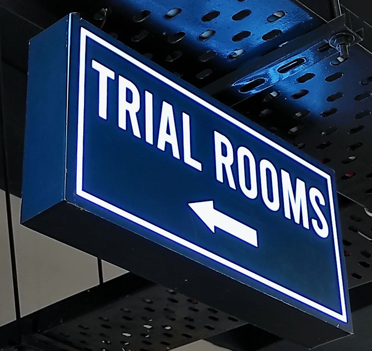 Blue illuminated Trial Rooms directional sign used as a branded retail fixture.