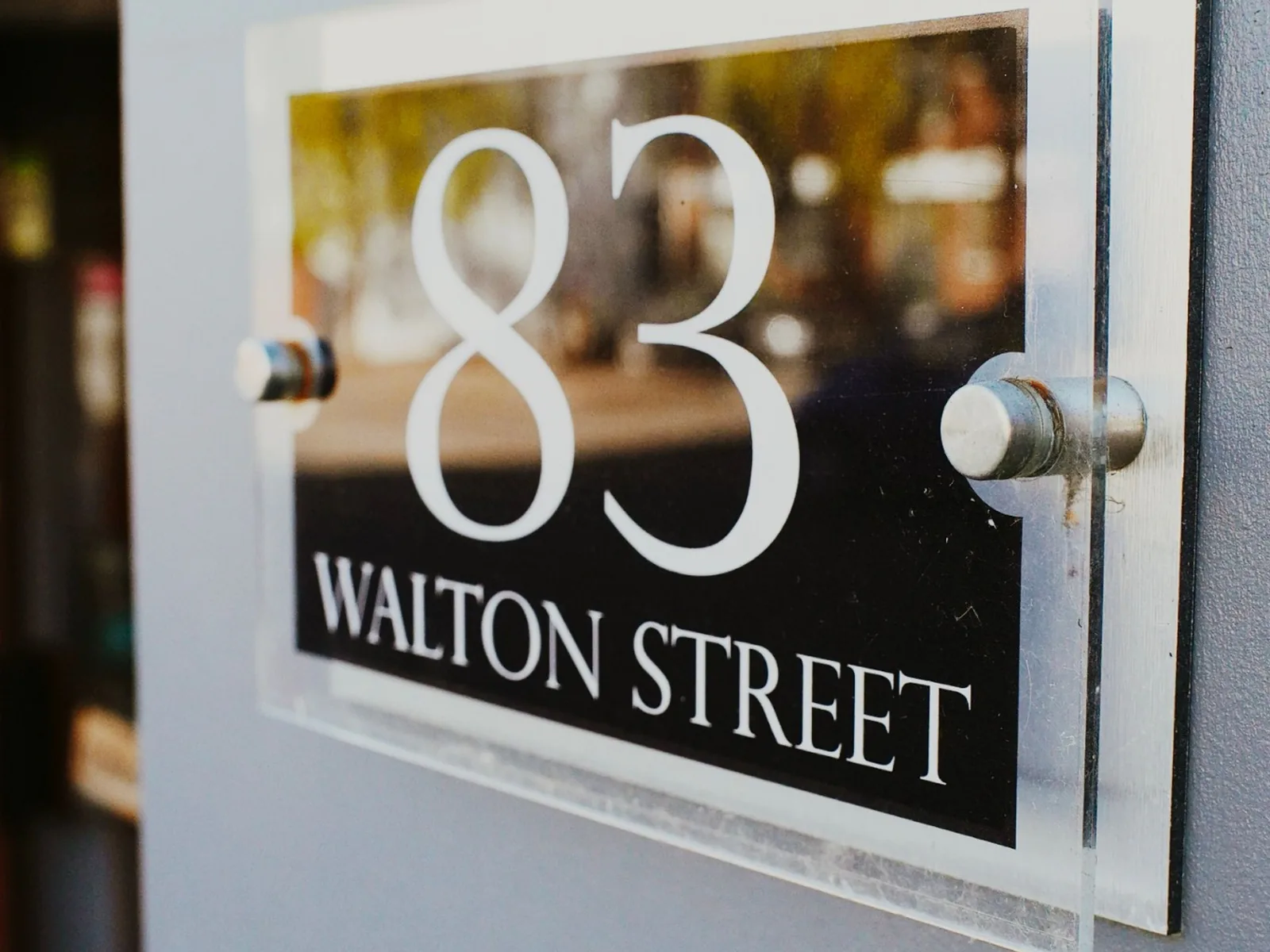 Clear wall-mounted acrylic sign face with polished edges and metal stand-off fixings.