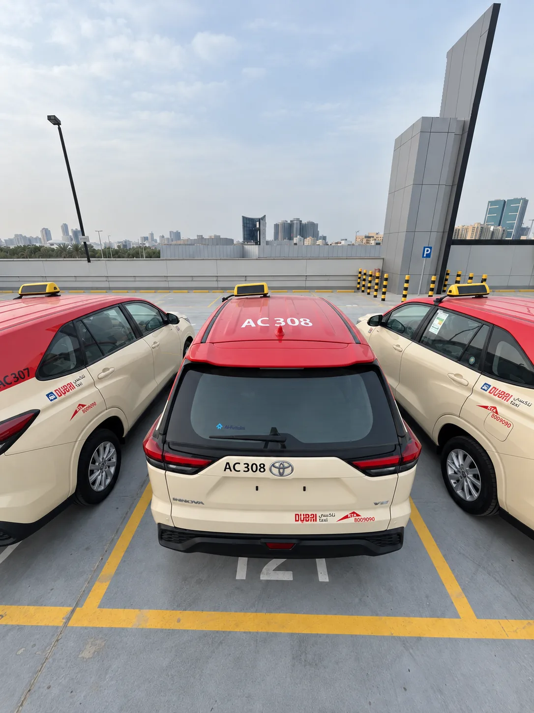 Three Dubai Taxi cars in red and cream livery parked side by side, seen from above the rear.