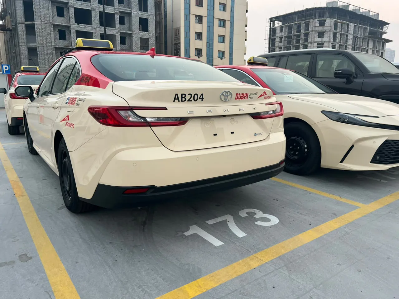 Rear of Dubai Taxi Toyota Camry AB204 with its fleet number, parked beside more cars from the fleet.